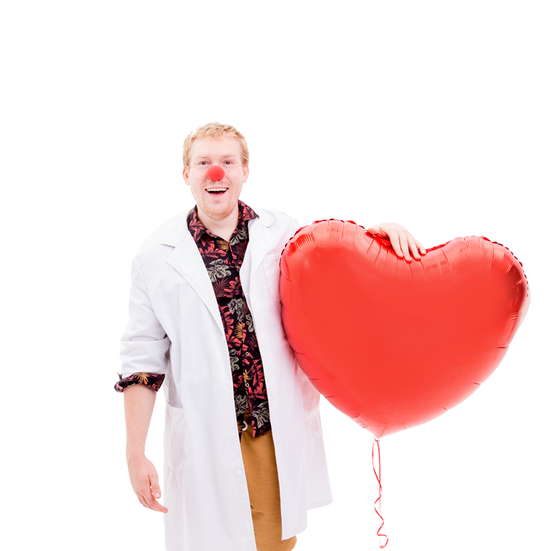 Egy fiatal bohócdoktor egy óriási felfújható piros szívlufit tart a kezében.